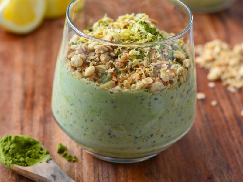 Green matcha overnight oats in a glass cup topped with granola and lemon zest on a wooden cutting board