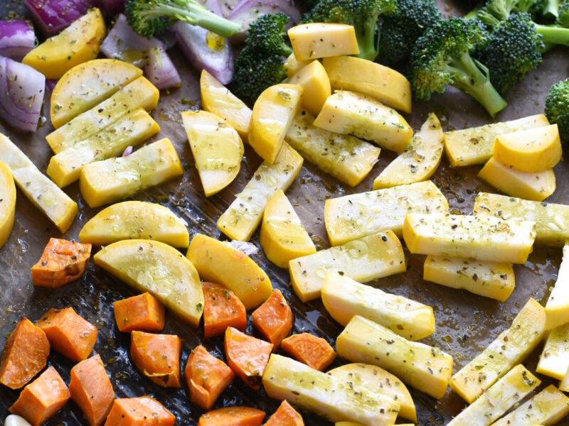 raw vegetables on a baking sheet Raw chopped vegetables on baking sheet including broccoli,yellow squash, red onion, sweet potato and garlic cloves.