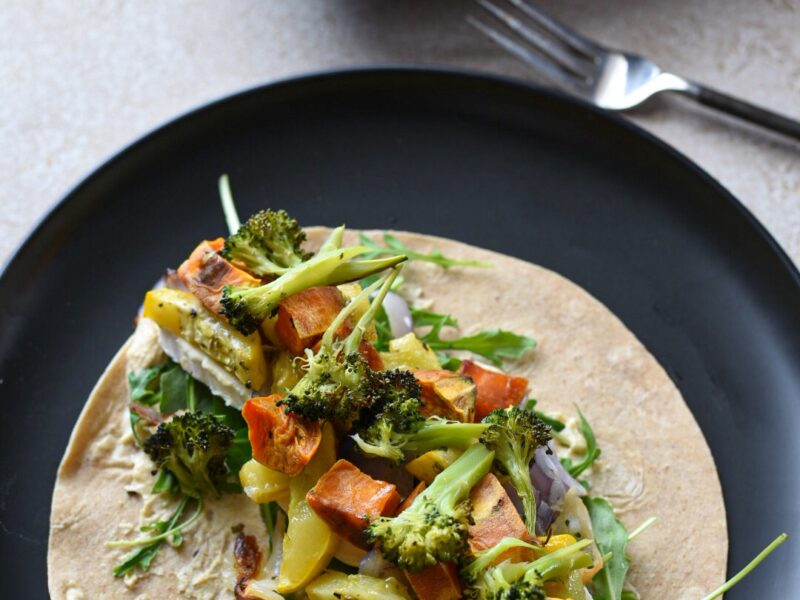 roasted vegetable wrap recipe A black plate topped with an open roasted veggie hummus wrap.