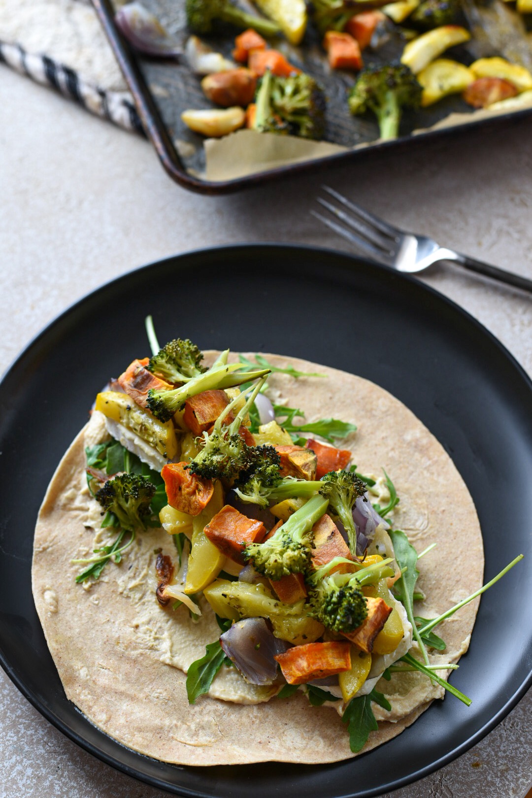 roasted vegetable wrap recipe A black plate topped with an open roasted veggie hummus wrap.