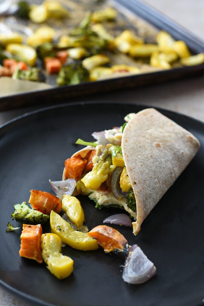 A roasted veggie wrap with hummus on a black plate with a bite taken out of it.
