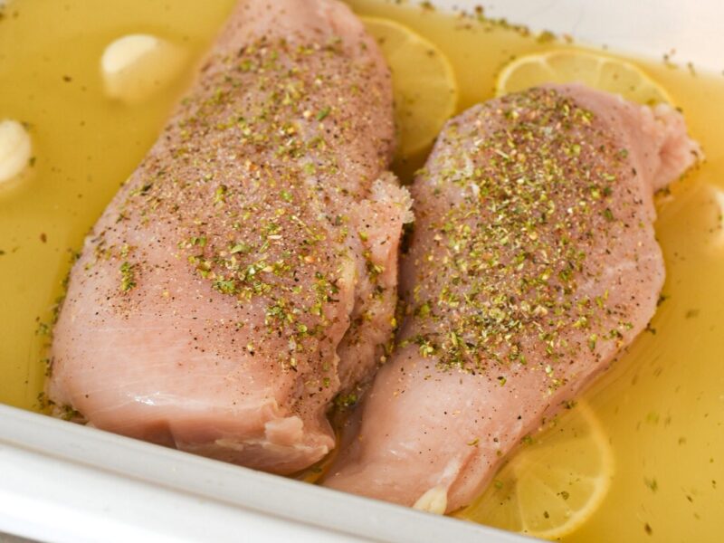 seasoned lemon chicken breasts Seasoned chicken breasts on top of lemon slices surrounded by garlic cloves and broth in a slow cooker.