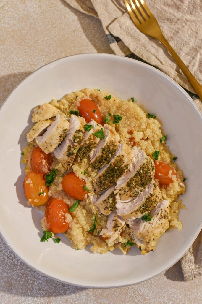 A bowl filled with slow cooker lemon chicken and quinoa with cherry tomatoes.