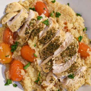 Close up of sliced herb chicken breast on quinoa surrounded by cherry tomatoes and parsley