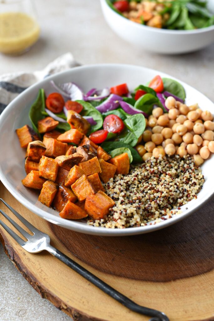 The ingredients for sweet potato quinoa salad in a bowl with roasted sweet potato, chickpeas, quinoa, spinach, red onion and tomato.