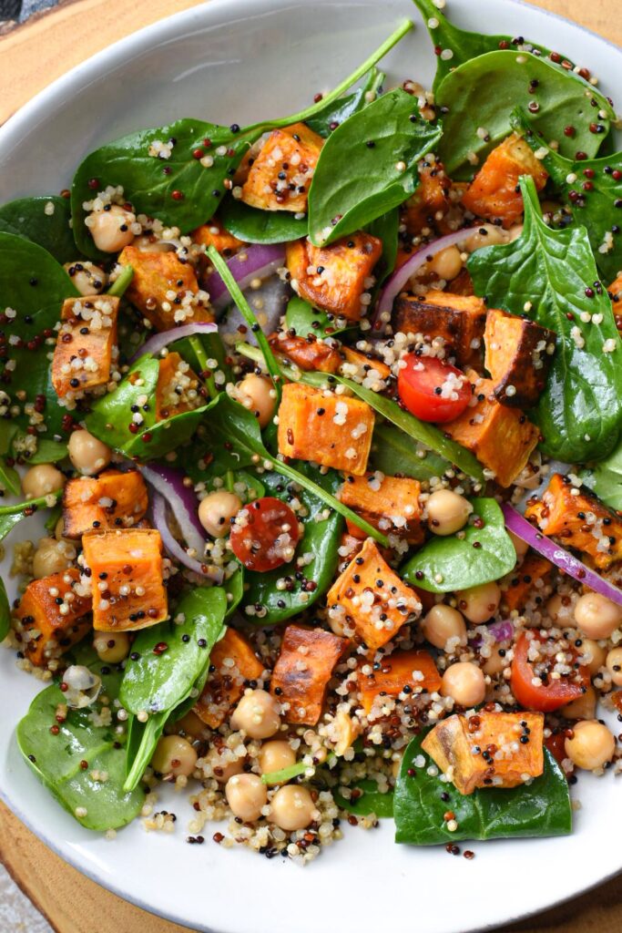 An overhead shot of sweet potato quinoa salad mixed with baby spinach, tomatoes, red onion and chickpeas.
