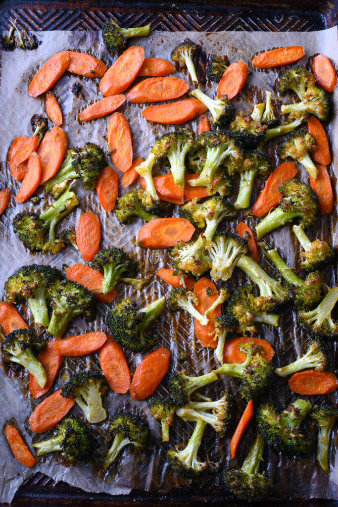 A baking sheet filled with roasted broccoli and carrots over parchment paper.