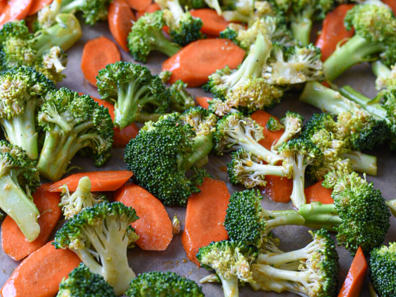 Raw carrots and broccoli on a baking sheet with a honey mustard sauce on it