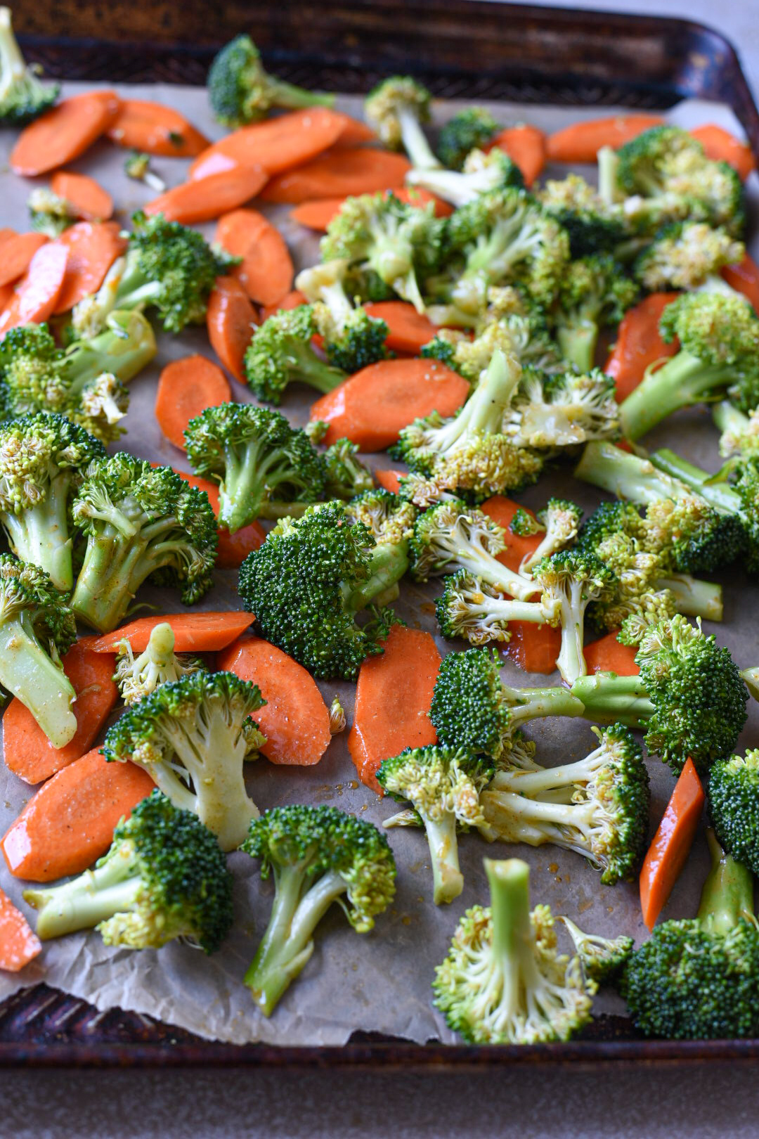 Raw carrots and broccoli on a baking sheet with a honey mustard sauce on it