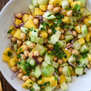 An overhead shot of cucumber mango salad with chickpeas and red onion in a white bowl