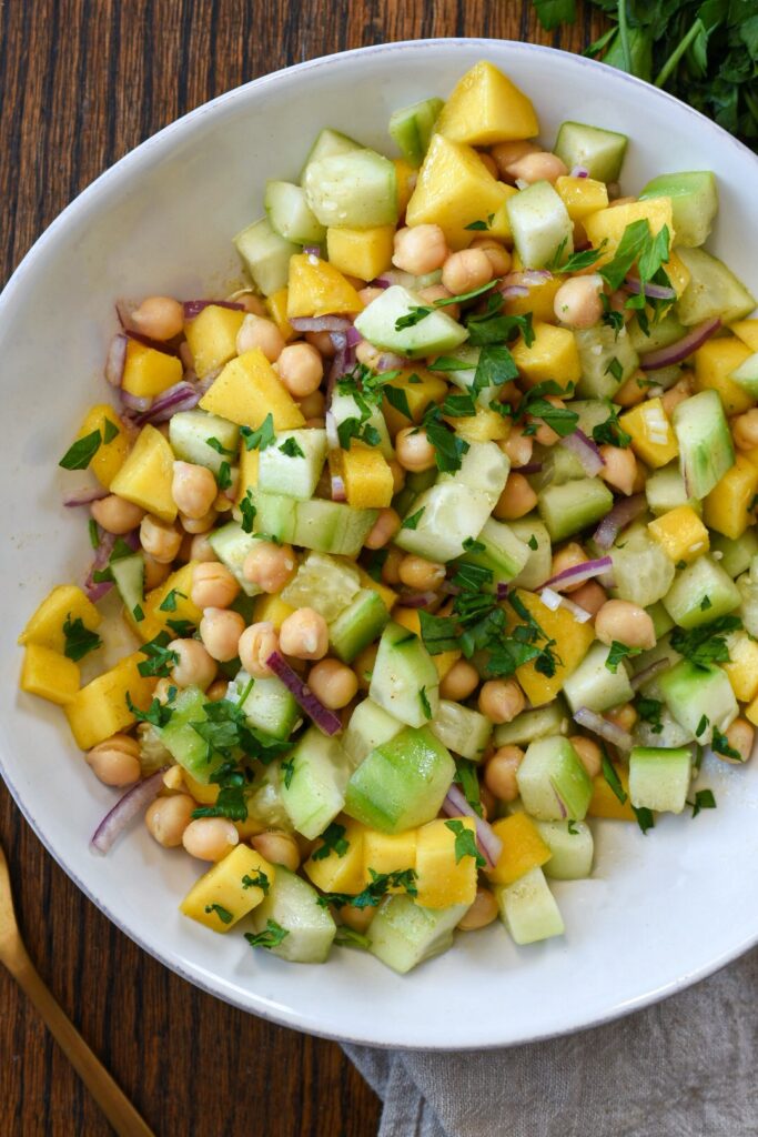 An overhead shot of cucumber mango salad with chickpeas and red onion in a white bowl