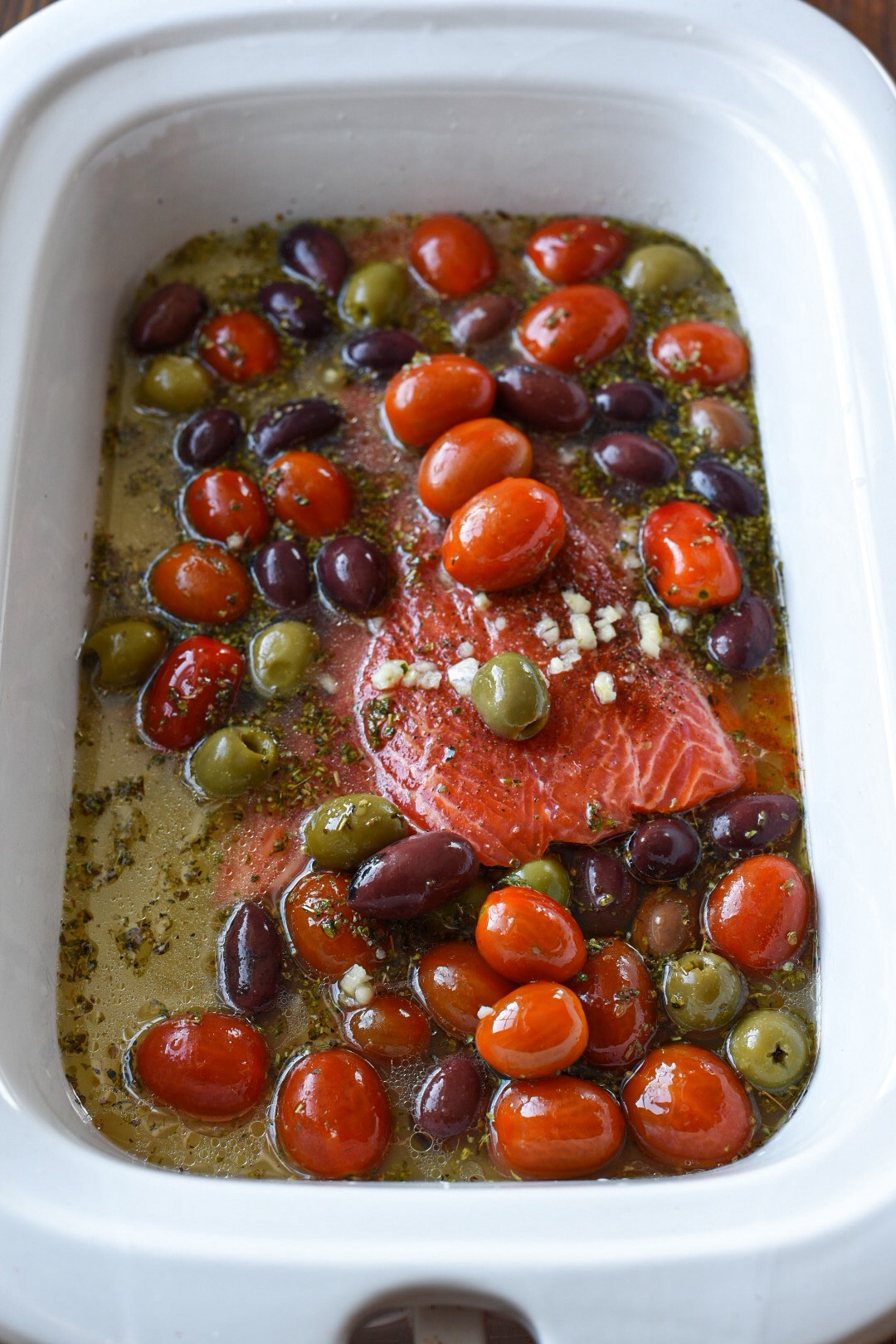 Raw salmon in a slow cooker with a lemon broth, olives and tomatoes