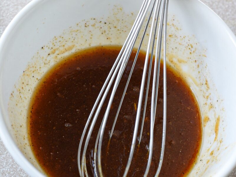 A white bowl filled with a honey mustard sauce for broccoli and carrots after it was whisked