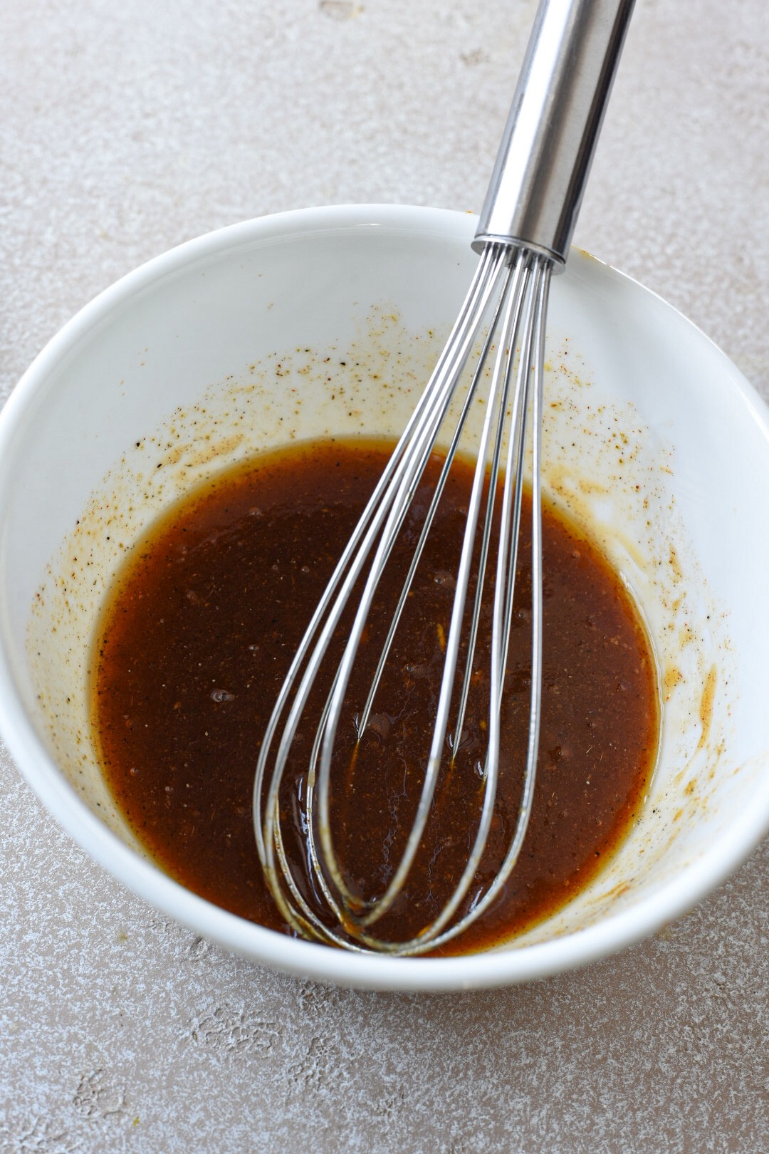 A white bowl filled with a honey mustard sauce for broccoli and carrots after it was whisked