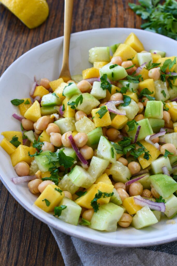A white bowl filled with cucumber mango salad with chickpeas and red onion