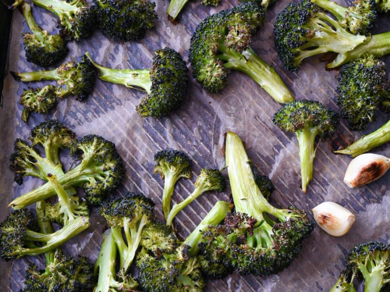 Roasted broccoli and garlic cloves on a baking sheet.