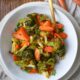 An overhead shot of a bowl filled with roasted broccoli and carrots with raw carrots in the corner
