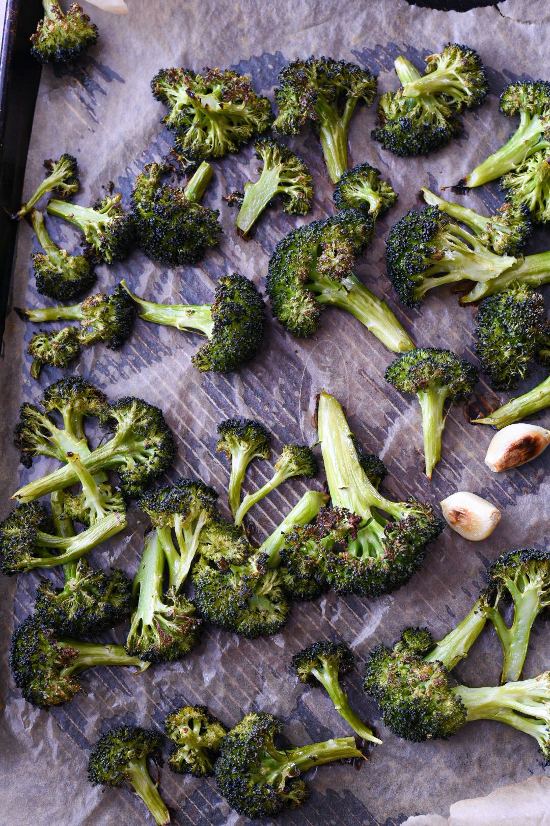 Roasted broccoli and garlic cloves on a baking sheet.