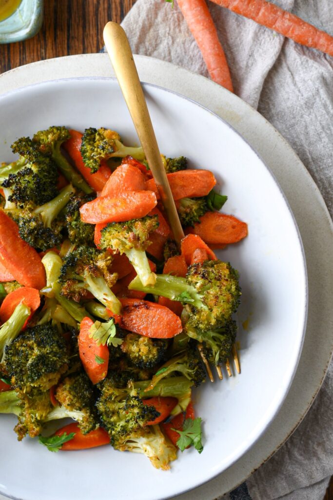 A close up overhead shot of a white bowl filled with roasted broccoli and carrots with honey dijon sauce
