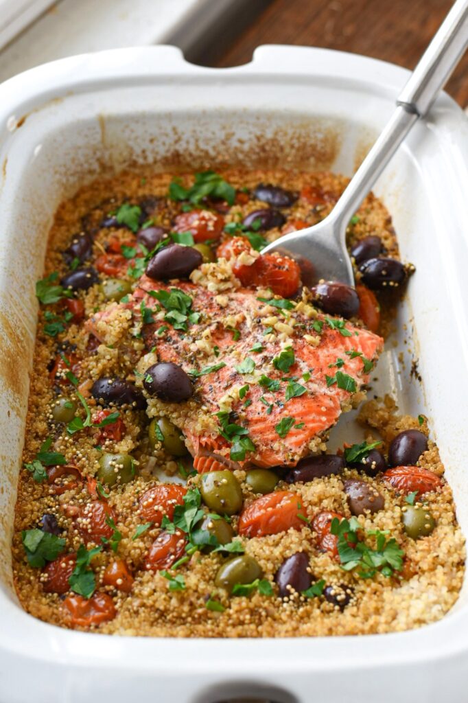salmon in a slow cooker with olives, tomatoes and quinoa being lifted out by a spatula