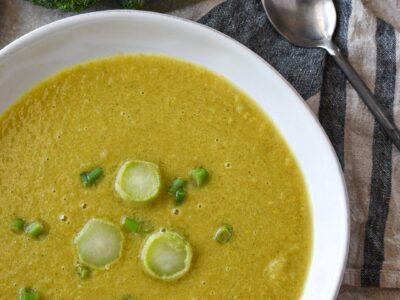 A close image of curried broccoli stem soup in a white bowl with green onion