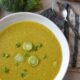 A close image of curried broccoli stem soup in a white bowl with green onion