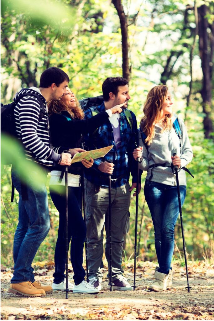 Two men and two women hiking in the woods and smiling as they point to something in the distance
