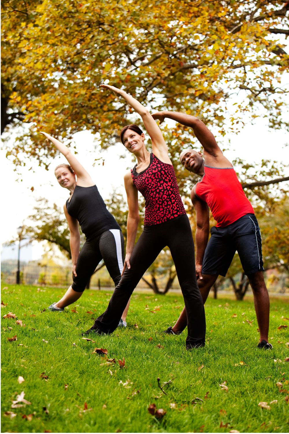 group of happy people exercising Three people in a park doing yoga and stretching to the side