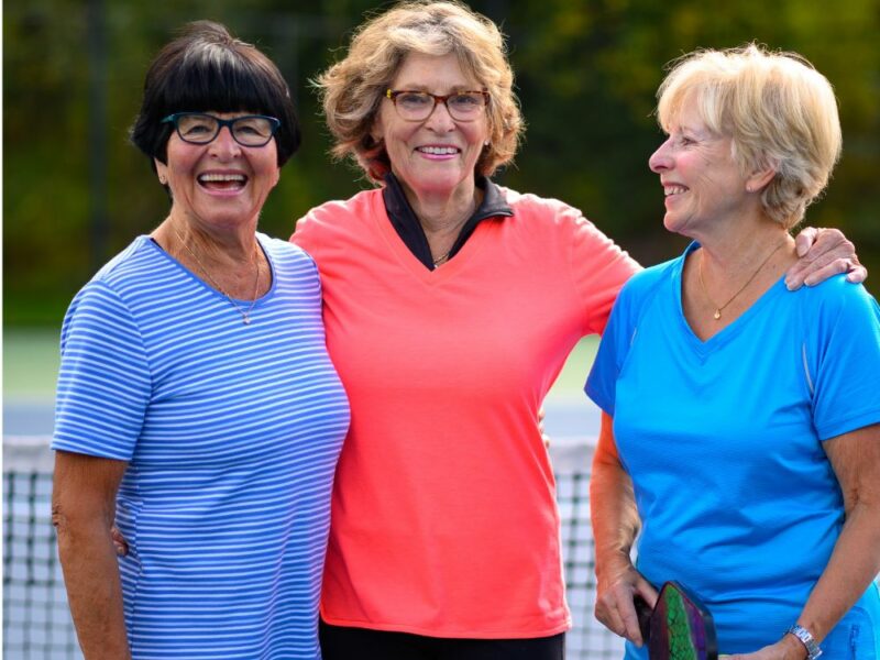 Three older ladies playing pickleball together and smiling
