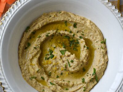 An overhead shot of hummus without tahini in a white bowl with carrot sticks next to it and minced mint leaves on top.