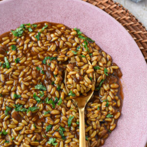 A pink plate filled with a kamut instant pot recipe with a gold spoon and parsley on the kamut