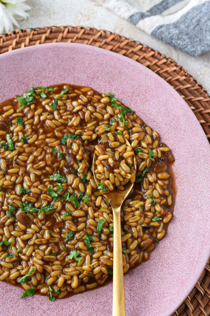 A pink plate filled with a kamut instant pot recipe with a gold spoon and parsley on the kamut