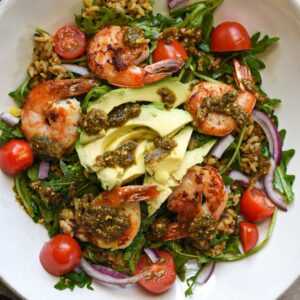 A close up overhead image of a shrimp and pesto buddha bowl with rice, quinoa, red onion, and tomatoes.