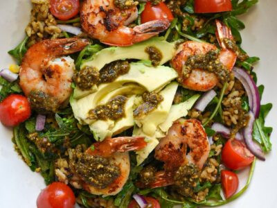 A close up overhead image of a shrimp and pesto buddha bowl with rice, quinoa, red onion, and tomatoes.