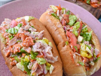A chopped italian sandwich on a pink plate with italian sandwich dressing in the background