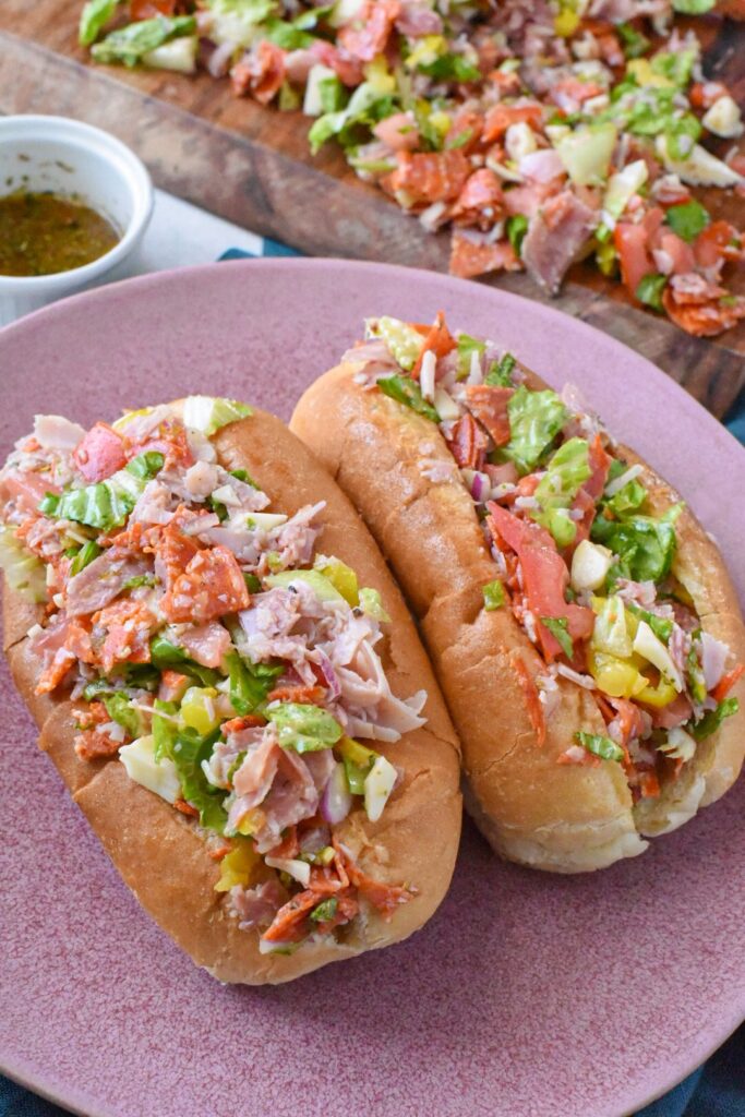 A chopped italian sandwich on a pink plate with italian sandwich dressing in the background