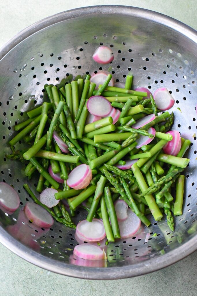 Blanched asparagus and radishes in a colander.