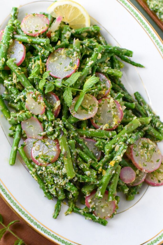 A close up of blanched asparagus salad with radishes and a gremolata sauce
