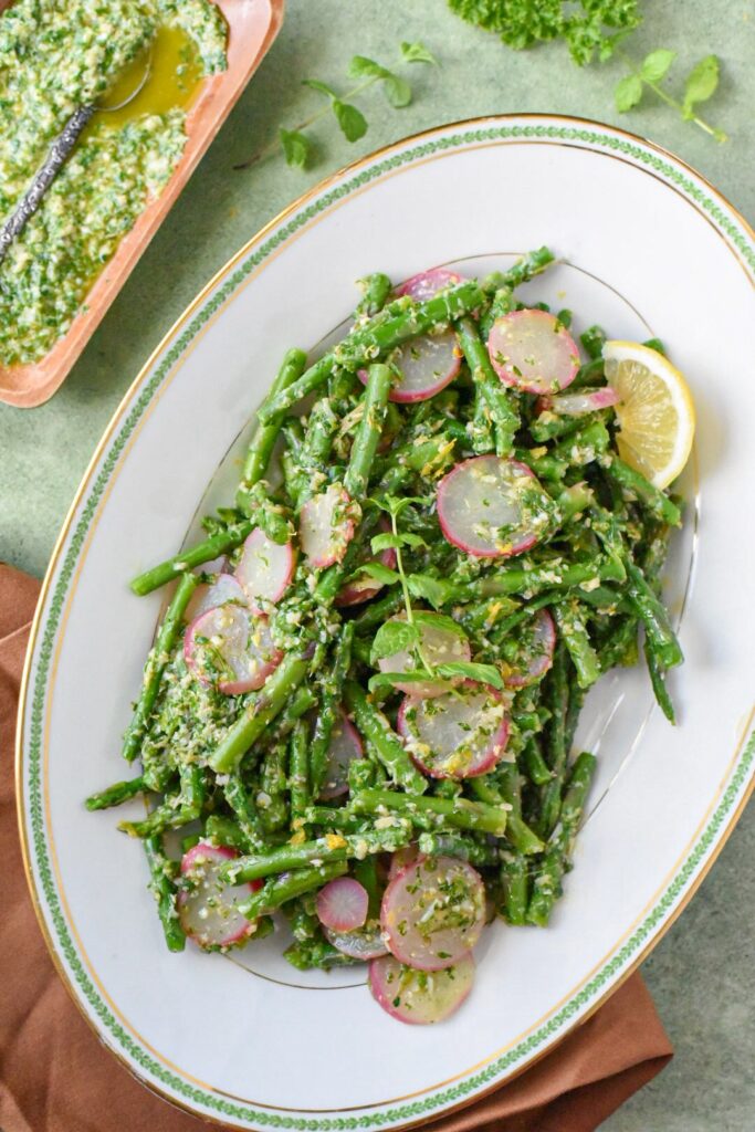 An overhead image of blanched asparagus salad with mint gremolata sauce on a white serving platter