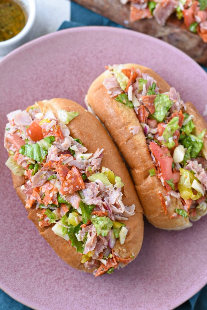 Two italian chopped sandwiches on a pink plate filled with deli meats.