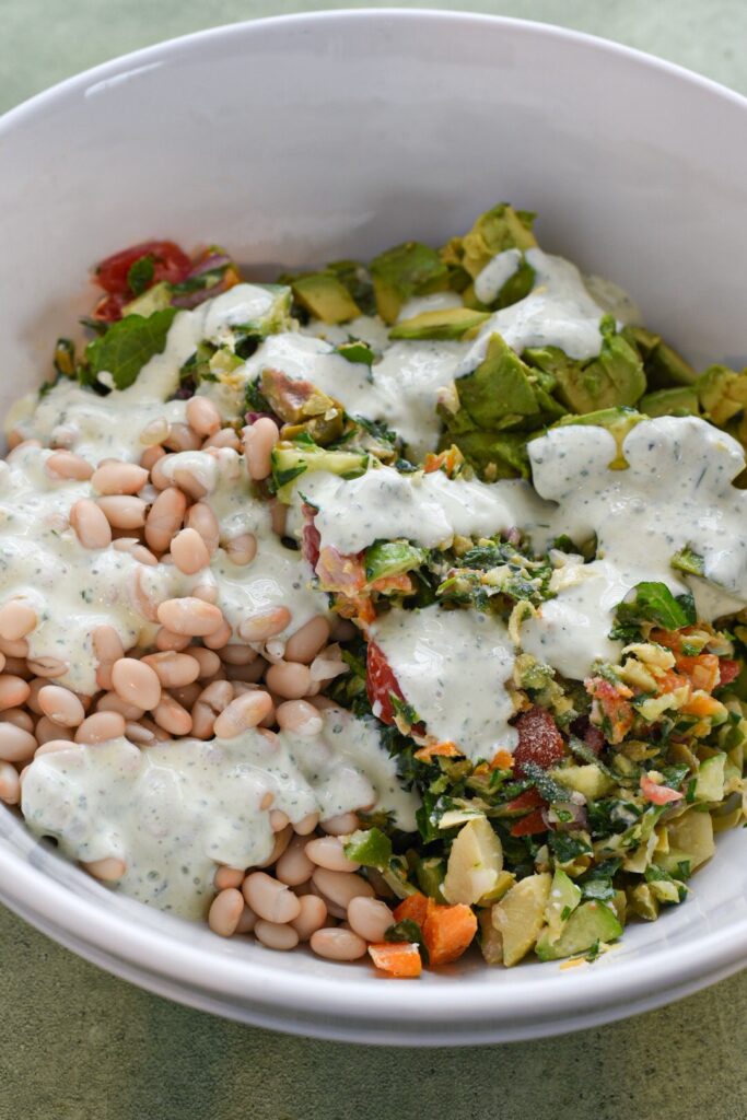 Mediterranean sandwich salad in a white bowl drizzled with homemade ranch dressing