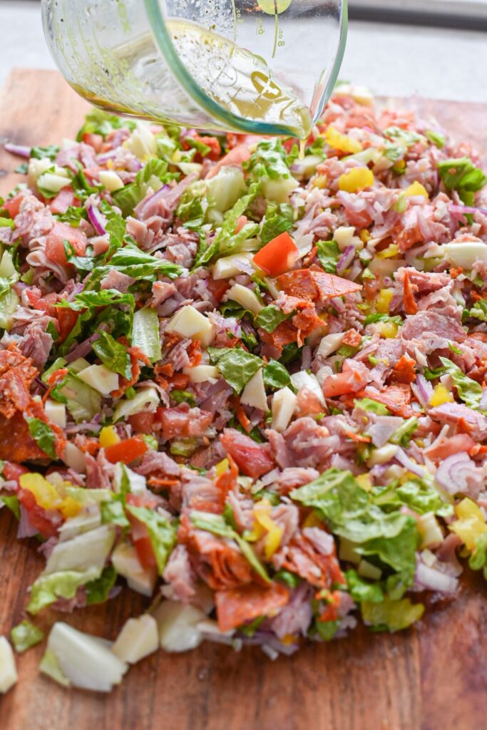 chopped sandwich recipe (1) Pouring italian dressing over the chopped ingredients for a sandwich.