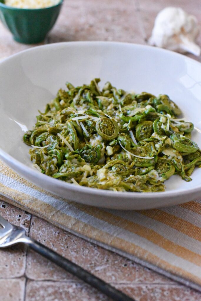 Garlic parmesan fiddleheads in a white bowl with a yellow and white striped napkin under it