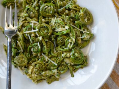 Fiddleheads in a white bowl with parmesan cheese and a fork