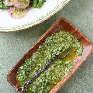 An herb gremolata sauce in a wooden serving dish with an old silver spoon