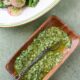 An herb gremolata sauce in a wooden serving dish with an old silver spoon