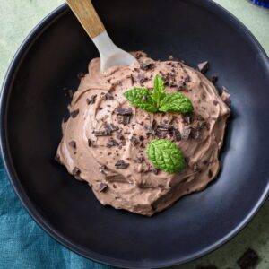 A close up of a black bowl filled with greek yogurt chocolate mousse, topped with shaved chocolate and mint leaves