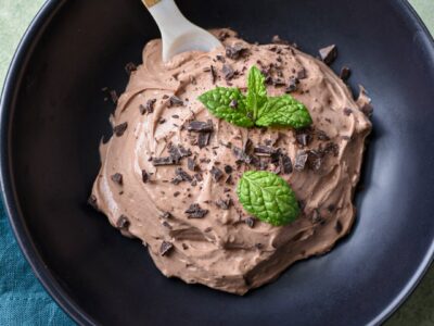 A close up of a black bowl filled with greek yogurt chocolate mousse, topped with shaved chocolate and mint leaves