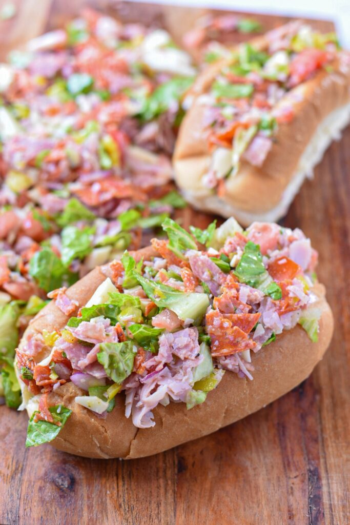 A chopped italian sandwich on a cutting board filled with chopped ingredients