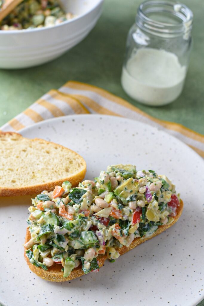 mediterranean chopped salad on bread A Mediterranean chopped sandwich on a white plate with homemade ranch dressing in the background